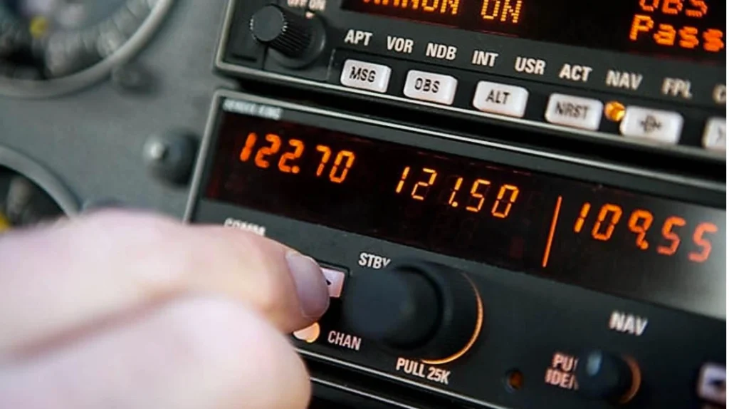 A imagem mostra um piloto operando equipamentos de rádio e navegação no painel de um avião