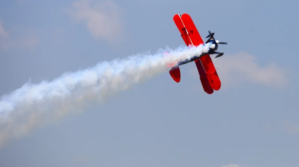 A imagem mostra a apresentação de uma aeronave de acrobacia soltando fumaça e executando manobras